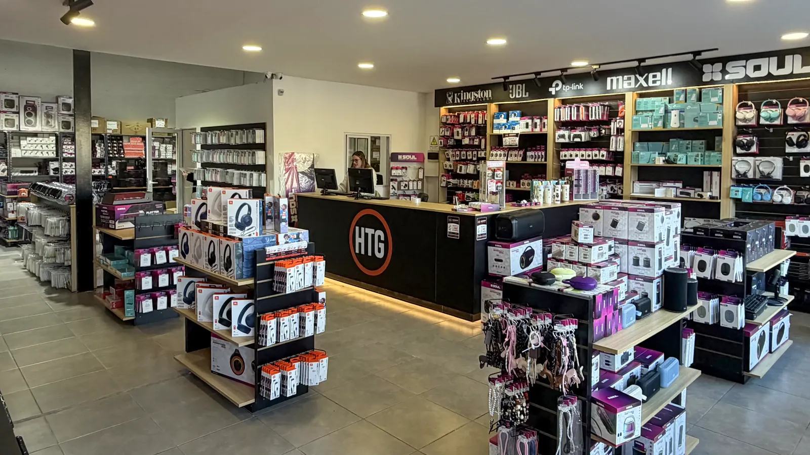 Salón mayorista de HTG: el mostrador con el logo y la pared de marcas Kingston, JBL, TP-Link, Maxell y SOUL